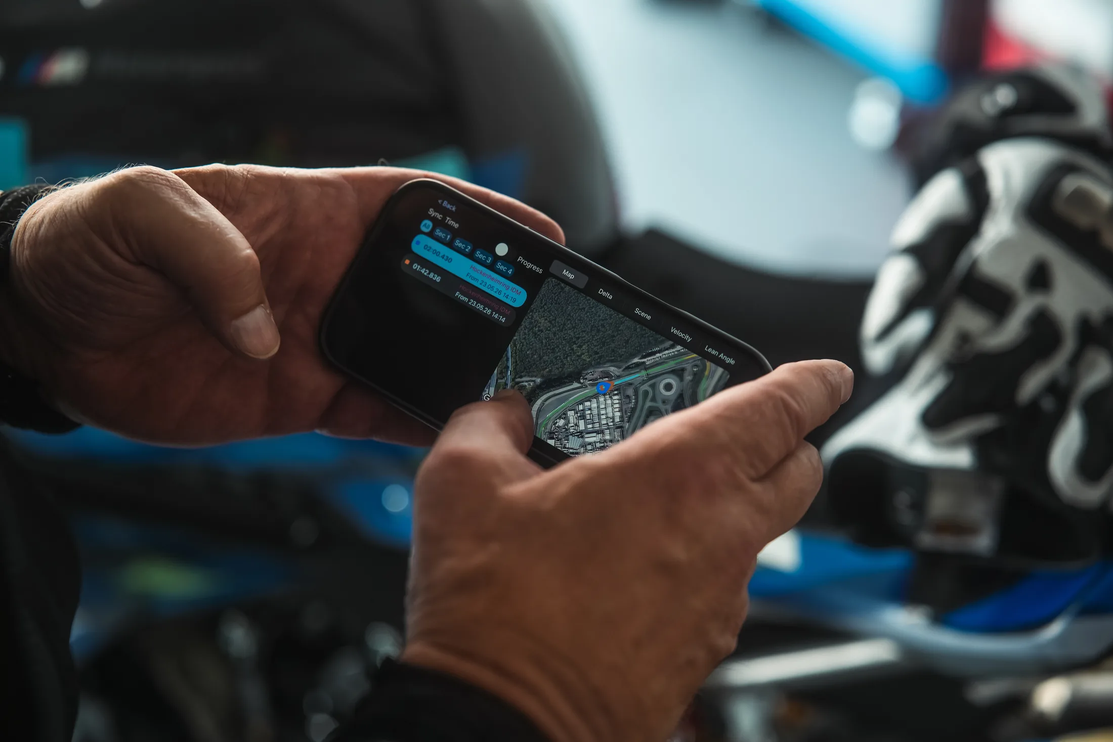 Hands reviewing circuit and lap data on a phone beside a motorcycle